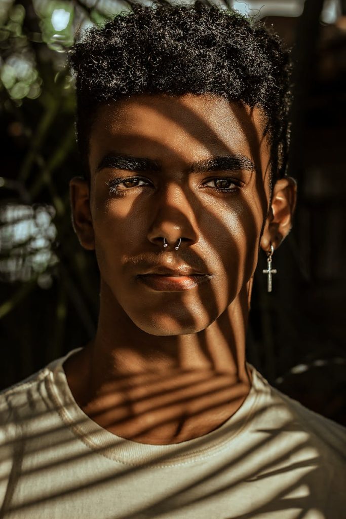 Jeune homme élégant avec des ombres sur le visage, portant des boucles d'oreilles et un piercing au septum.