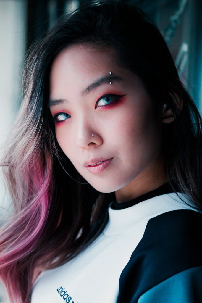 Portrait stylisé d'une femme asiatique au maquillage des yeux vibrant et aux mèches de cheveux roses, mettant en valeur la mode moderne.