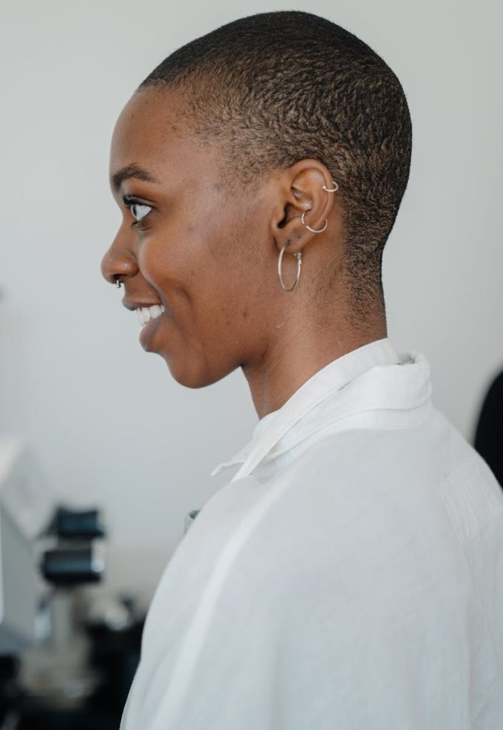 Vue de côté d'un jeune aux cheveux courts et aux piercings, en chemise blanche, souriant.