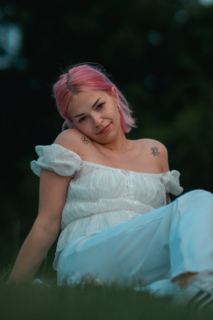 une femme aux cheveux roses assise dans l'herbe